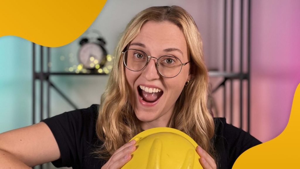 Uśmiechnięta blondynka w czarnej koszulce ściska rękami żółty hełm - szkolenia bhp online Power Safety